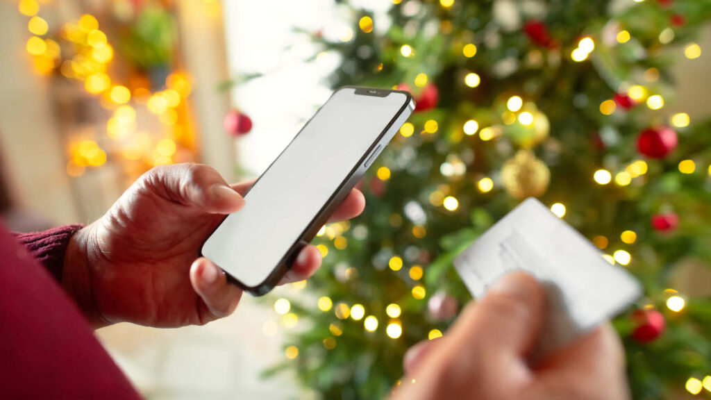 Person holding mobile phone beside Christmas tree