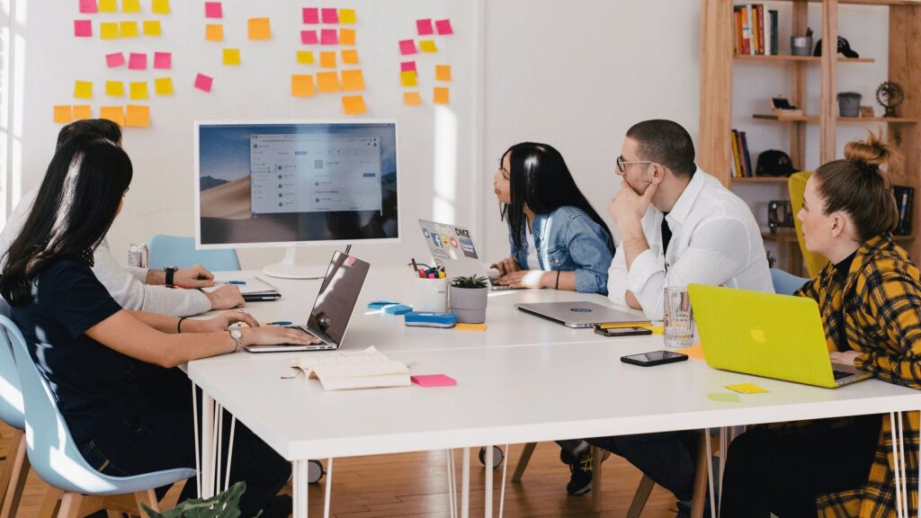 How to write an employee engagement survey: Employees sitting around desk watching video screen